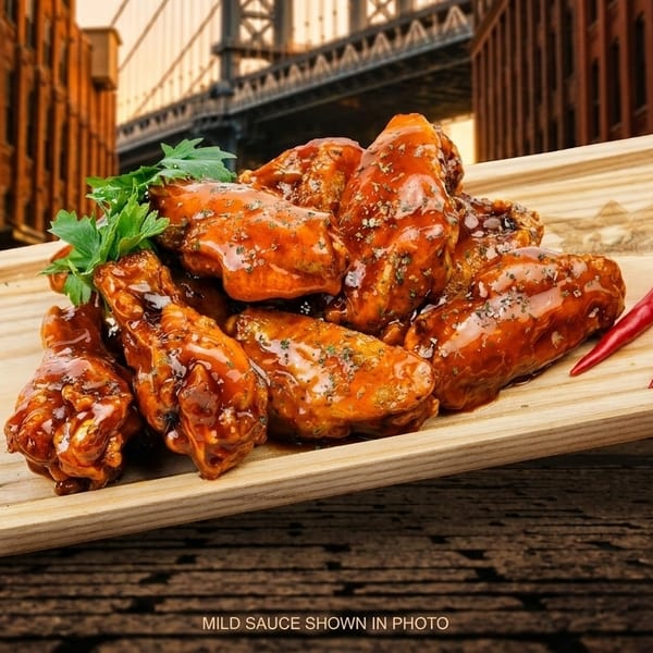 Mild sauce chicken wings with parsley and red chilies on a wooden tray, with a city background.
