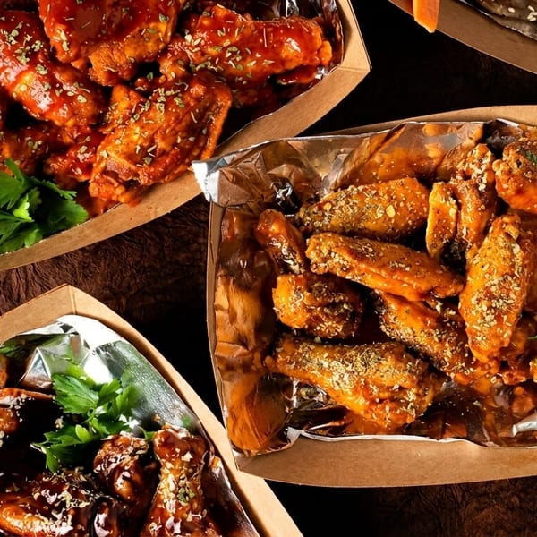 Three foil-lined cardboard trays filled with various flavors of chicken wings, garnished with parsley.