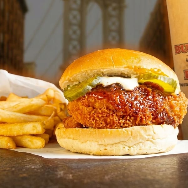Buffalo Boss chicken sandwich with fries and a branded drink cup against a city backdrop.